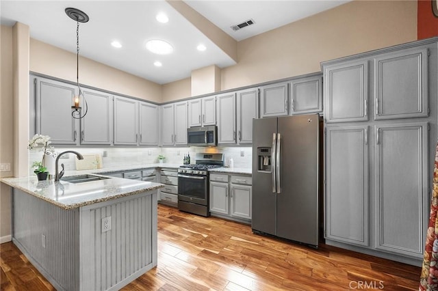kitchen featuring a peninsula, light stone countertops, gray cabinets, a sink, and stainless steel appliances