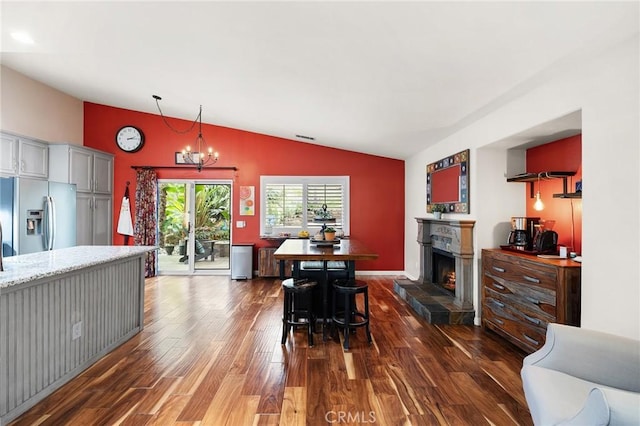interior space with visible vents, an inviting chandelier, wood finished floors, lofted ceiling, and a lit fireplace