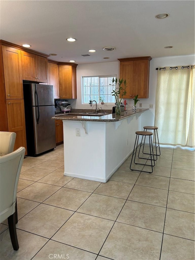 kitchen with a peninsula, a kitchen breakfast bar, light tile patterned flooring, freestanding refrigerator, and brown cabinetry