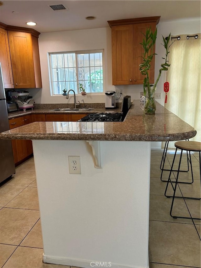 kitchen featuring brown cabinetry, a breakfast bar, a sink, and light tile patterned floors