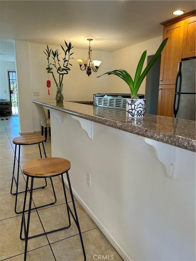 kitchen featuring dark stone counters, light tile patterned floors, a chandelier, brown cabinets, and a breakfast bar area