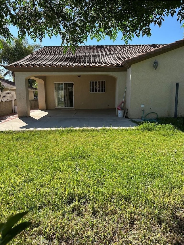 back of property with a yard, a tile roof, stucco siding, and fence
