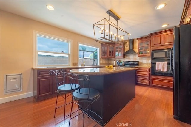 kitchen featuring wall chimney range hood, a center island, black appliances, a chandelier, and a breakfast bar