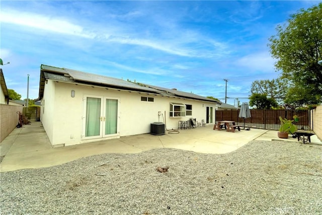 rear view of property with stucco siding, roof mounted solar panels, a fenced backyard, a patio area, and french doors