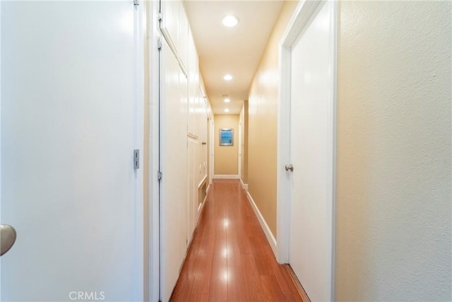 corridor featuring baseboards, recessed lighting, and light wood-style flooring