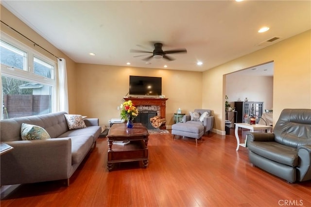 living area with ceiling fan, visible vents, wood finished floors, a fireplace with raised hearth, and recessed lighting