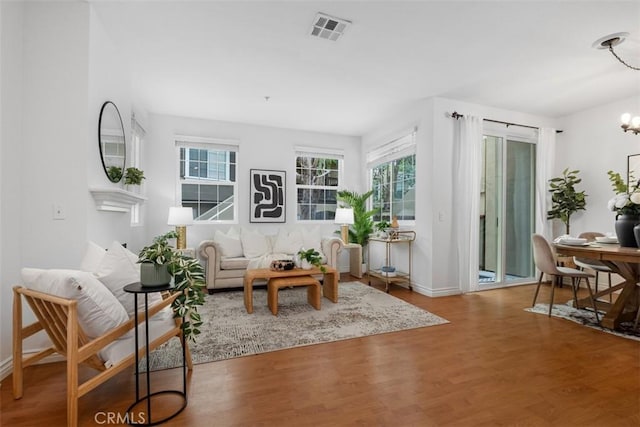 living area featuring wood finished floors, visible vents, a notable chandelier, and baseboards