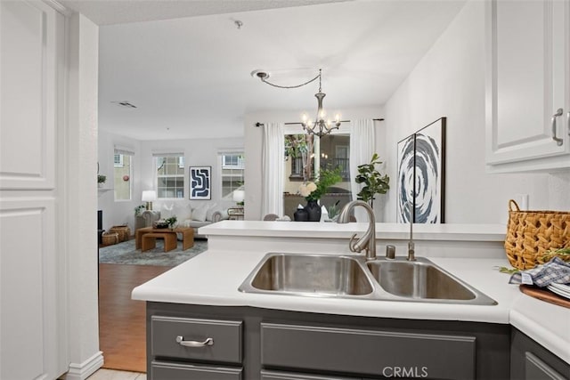 kitchen with white cabinetry, a sink, a chandelier, light countertops, and open floor plan