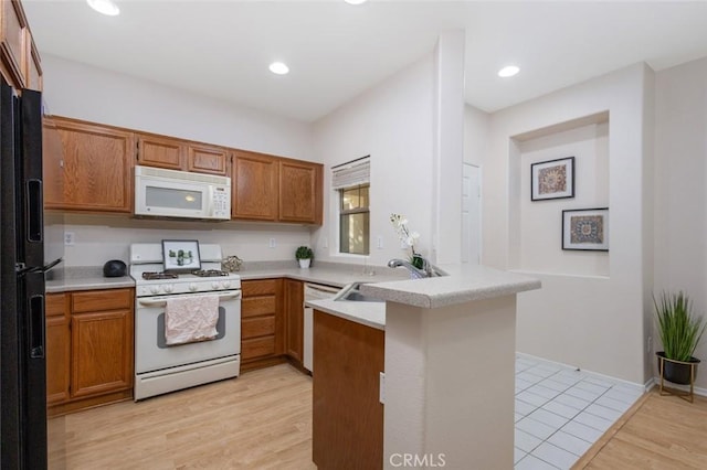 kitchen featuring brown cabinets, white appliances, a peninsula, and a sink