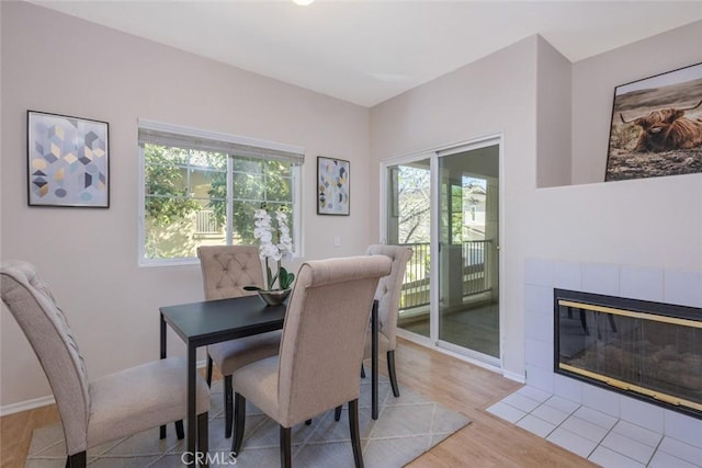 dining space featuring a tile fireplace, light wood finished floors, and baseboards