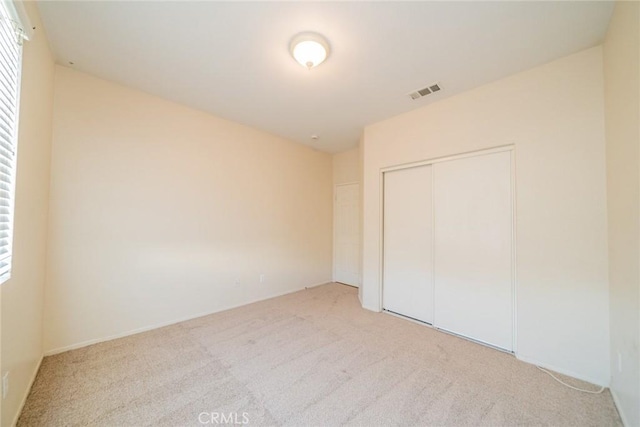unfurnished bedroom with light colored carpet, visible vents, and a closet