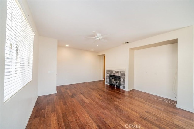 unfurnished living room with ceiling fan, visible vents, a fireplace, wood finished floors, and baseboards