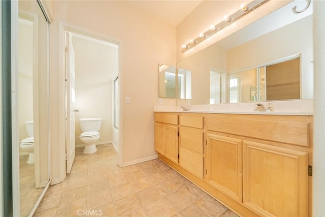 bathroom featuring double vanity, a sink, baseboards, bath / shower combo with glass door, and toilet