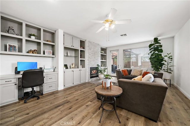 living area featuring built in desk, a fireplace, built in shelves, light wood-type flooring, and visible vents