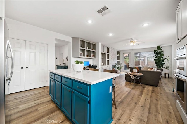 kitchen featuring visible vents, light wood-type flooring, a ceiling fan, blue cabinetry, and stainless steel appliances