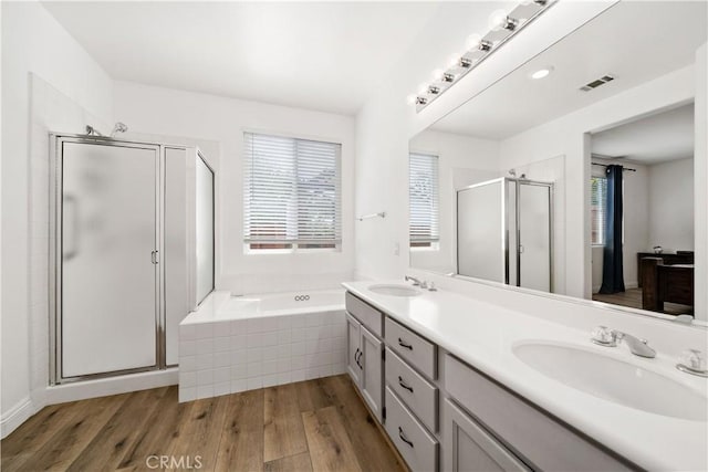 bathroom featuring double vanity, a bath, a shower stall, wood finished floors, and a sink