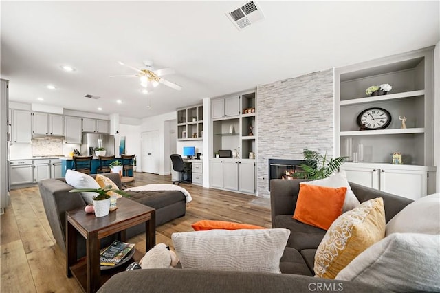 living area with light wood-style floors, a fireplace, a ceiling fan, and visible vents