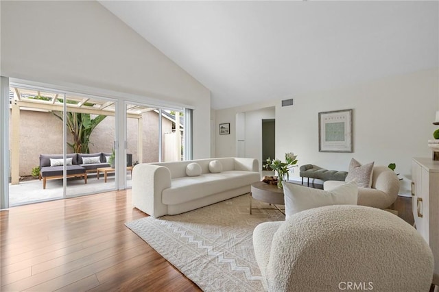 living area with high vaulted ceiling, wood finished floors, and visible vents