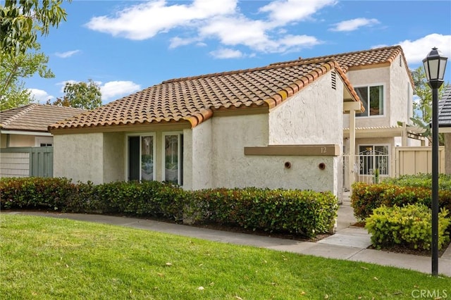 view of property exterior with stucco siding, a tile roof, fence, and a lawn