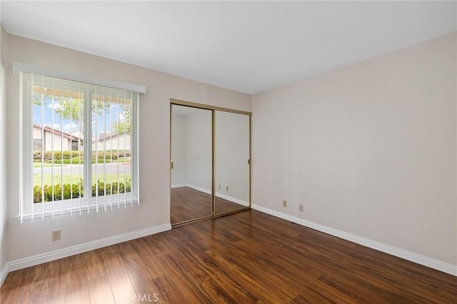 unfurnished bedroom featuring baseboards, dark wood-style floors, and a closet
