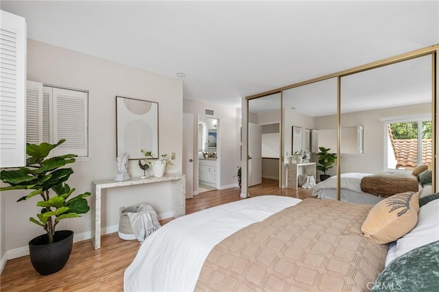 bedroom featuring visible vents, baseboards, ensuite bath, and wood finished floors