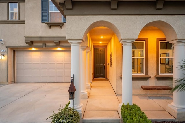 property entrance featuring concrete driveway, a garage, and stucco siding