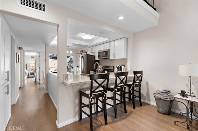 133 Morristown Ln, Costa Mesa, CA 92626 - kitchen with appliances with stainless steel finishes, baseboards, white cabinetry, a peninsula, and a breakfast bar area