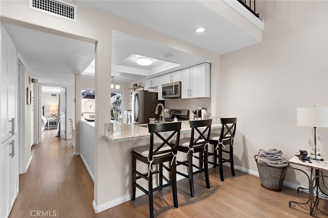 133 Morristown Ln, Costa Mesa, CA 92626 - kitchen with appliances with stainless steel finishes, white cabinets, a peninsula, a kitchen breakfast bar, and light wood-type flooring