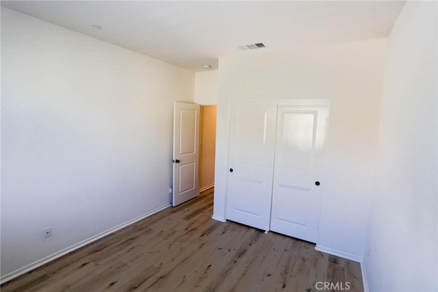 unfurnished bedroom featuring wood finished floors, a closet, baseboards, and visible vents