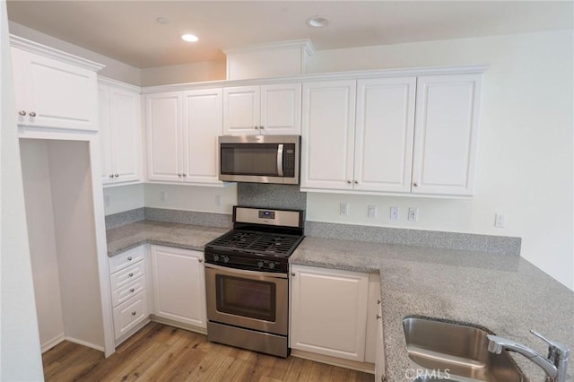 kitchen featuring white cabinets, recessed lighting, stainless steel appliances, a sink, and light wood-style floors