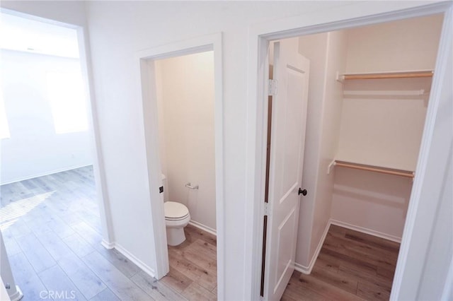 bathroom featuring baseboards, wood finished floors, a spacious closet, and toilet