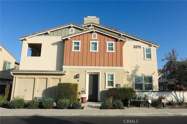 view of front of house featuring board and batten siding, a chimney, and stucco siding