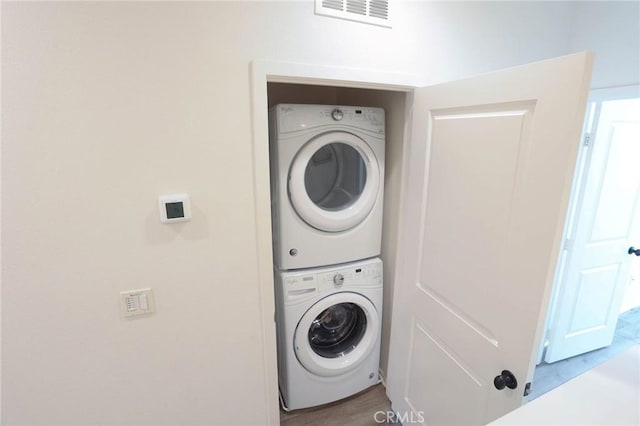 washroom featuring wood finished floors, visible vents, stacked washing maching and dryer, and laundry area