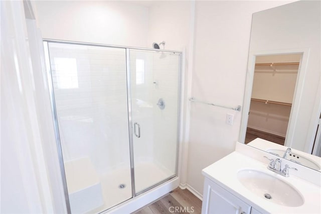 bathroom with a walk in closet, a shower stall, vanity, and wood finished floors