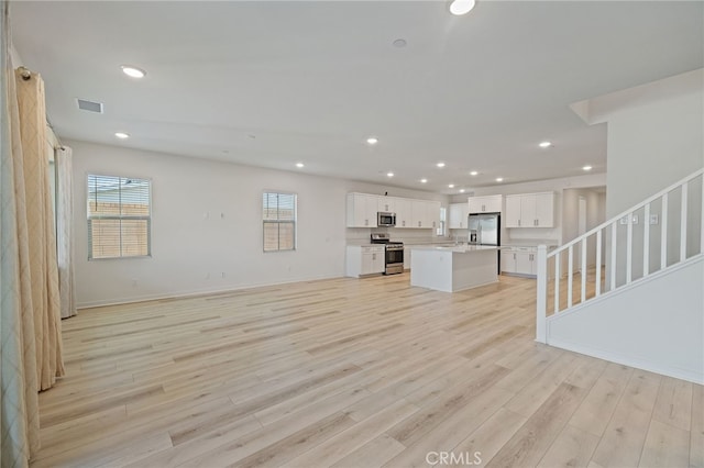 unfurnished living room featuring recessed lighting, stairway, light wood-style flooring, a sink, and visible vents