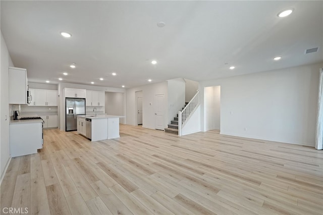 kitchen featuring open floor plan, an island with sink, light wood-style flooring, and stainless steel appliances