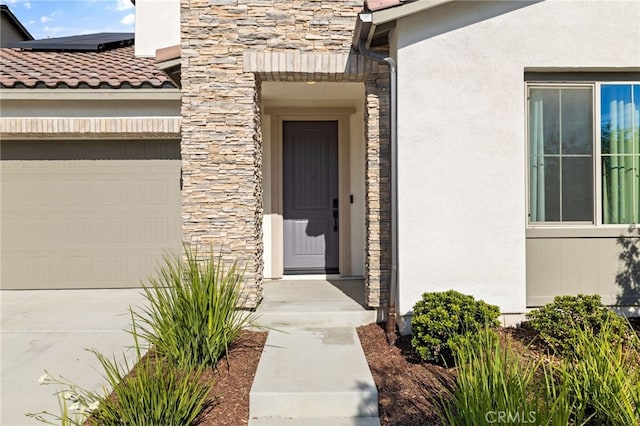 doorway to property with an attached garage, solar panels, stone siding, and stucco siding