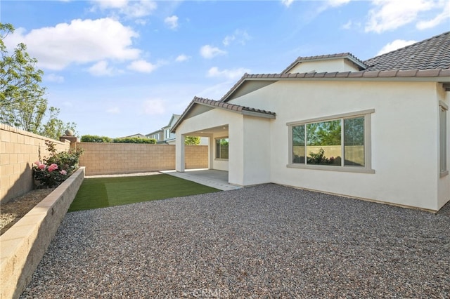 rear view of property with a tile roof, stucco siding, a fenced backyard, and a patio area