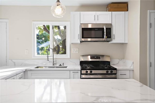 kitchen featuring light stone counters, white cabinetry, stainless steel appliances, and a sink