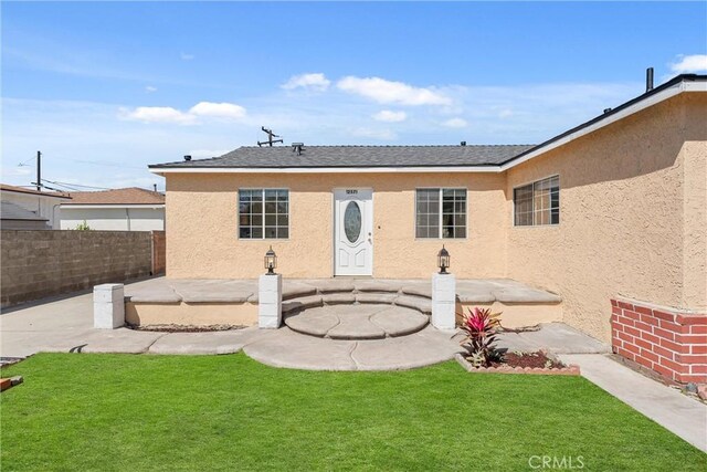 rear view of house featuring stucco siding, fence, a patio, and a lawn