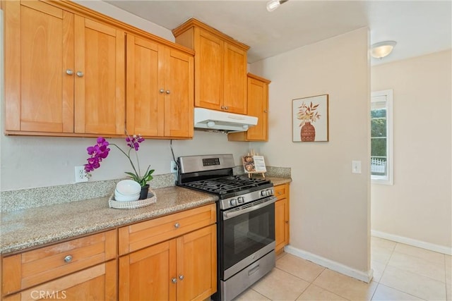 kitchen featuring stainless steel gas range, baseboards, light stone counters, under cabinet range hood, and light tile patterned floors