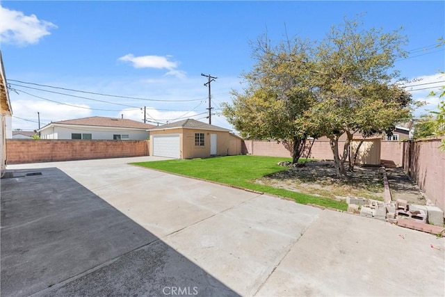 view of yard featuring concrete driveway, a fenced backyard, an outdoor structure, and a garage