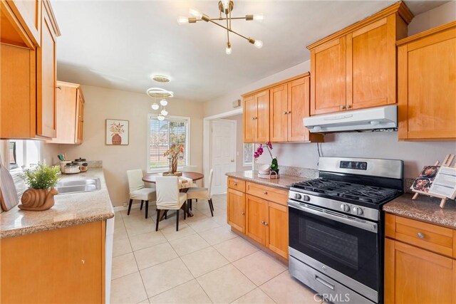 kitchen with light stone counters, under cabinet range hood, an inviting chandelier, light tile patterned flooring, and stainless steel range with gas cooktop