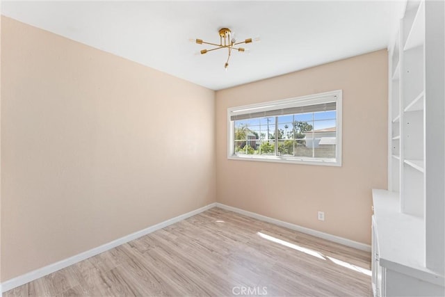 unfurnished room with an inviting chandelier, light wood-style floors, and baseboards