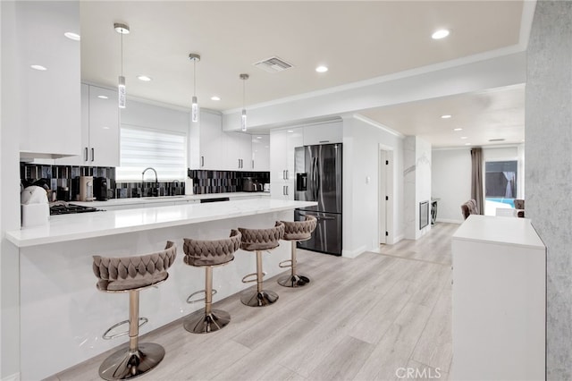 kitchen with visible vents, light countertops, white cabinets, a peninsula, and stainless steel fridge