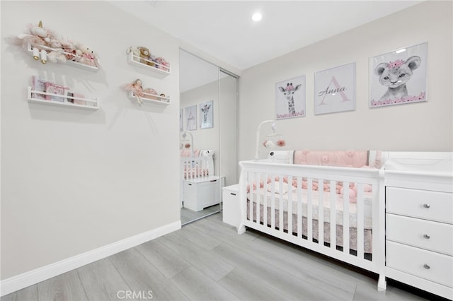 bedroom featuring a nursery area, wood finished floors, baseboards, a closet, and recessed lighting
