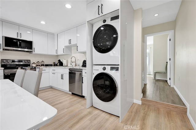 laundry room featuring laundry area, stacked washing maching and dryer, light wood-style flooring, recessed lighting, and baseboards