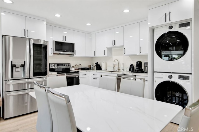 kitchen with white cabinets, a sink, appliances with stainless steel finishes, and stacked washing maching and dryer