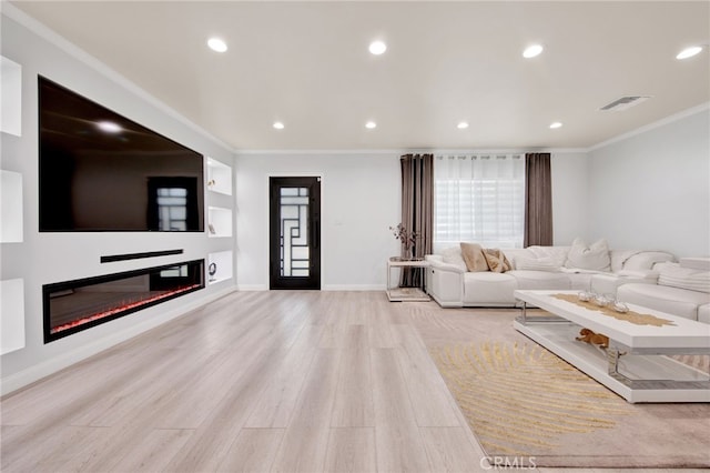 living room with visible vents, a glass covered fireplace, ornamental molding, and light wood-style flooring