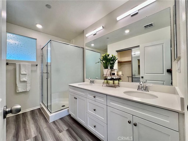 bathroom featuring a shower stall, double vanity, a sink, and wood finished floors